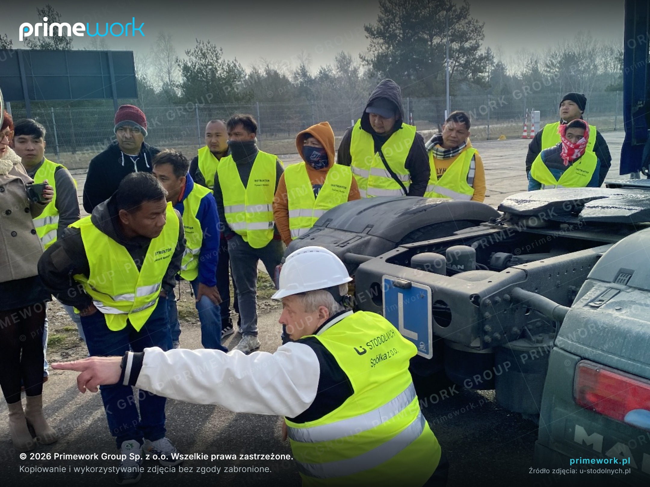 A group of Asian drivers in high-visibility vests during practical training at a semi-trailer