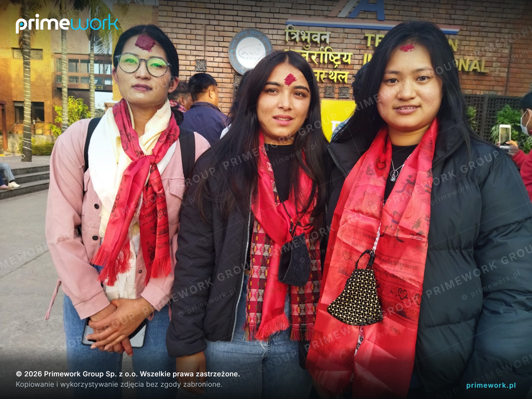 Trzy pracownice z Nepalu w czerwonych szalach przed terminalem odlotów w Katmandu